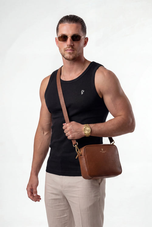 [Black] Man wearing sunglasses and a black tank top, holding a brown leather bag on a white background